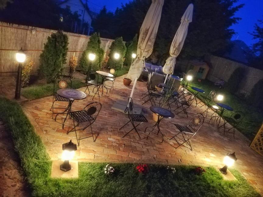 eine Terrasse mit Stühlen, Tischen und Lichtern in der Nacht in der Unterkunft Apartman Poirot in Érd