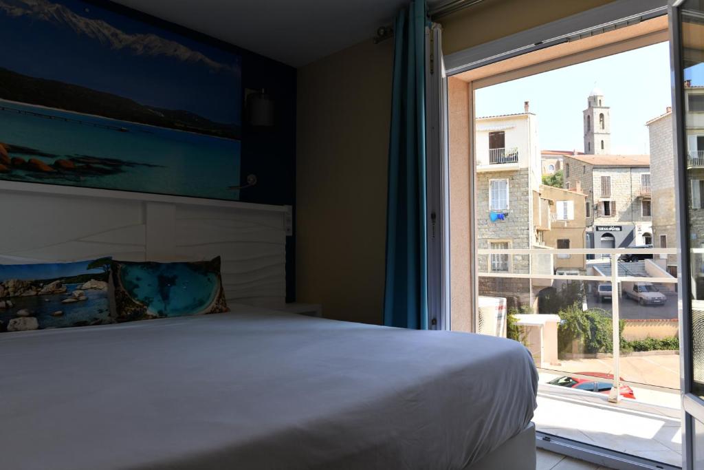 a bedroom with a bed and a large window at Hôtel Le Claridge in Propriano