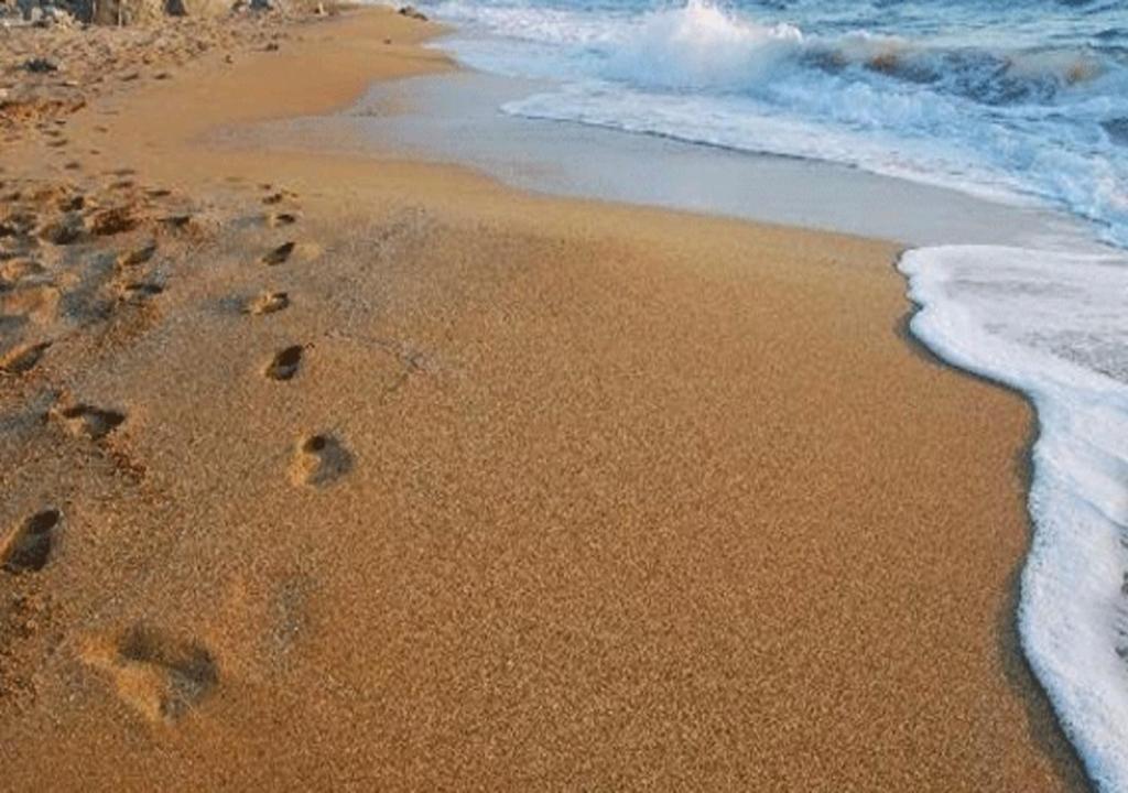 a beach with footprints in the sand and water at Galini Palace in Athens
