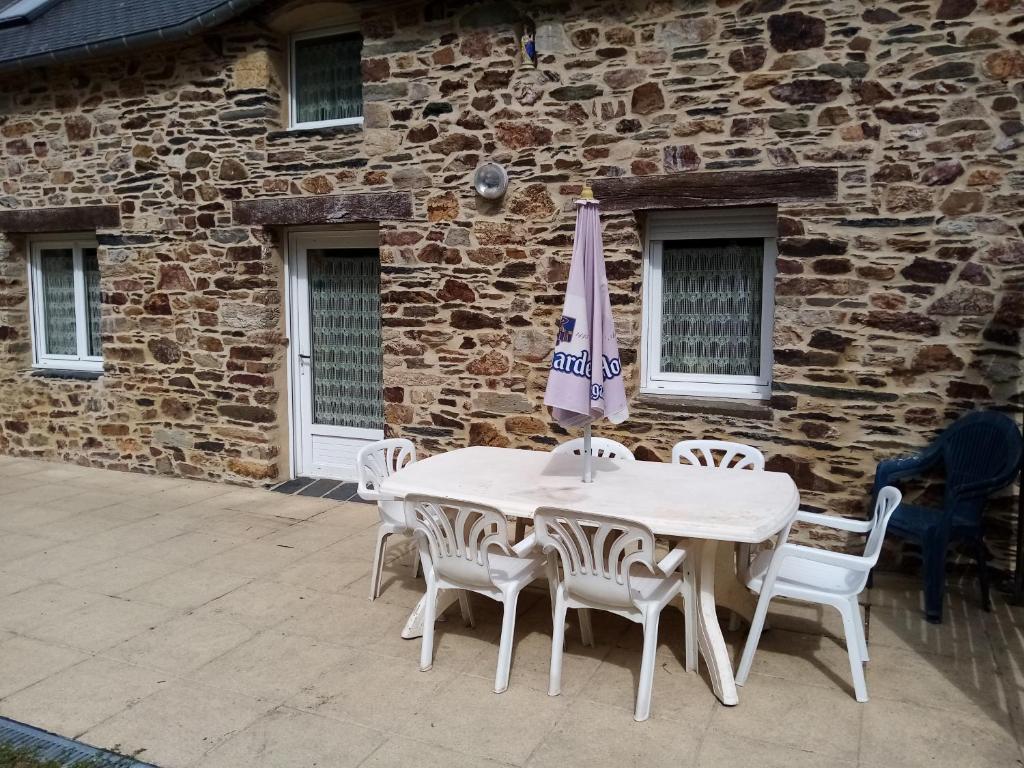 uma mesa branca e cadeiras com um guarda-sol em frente a um edifício em Gîte à la ferme em Merléac