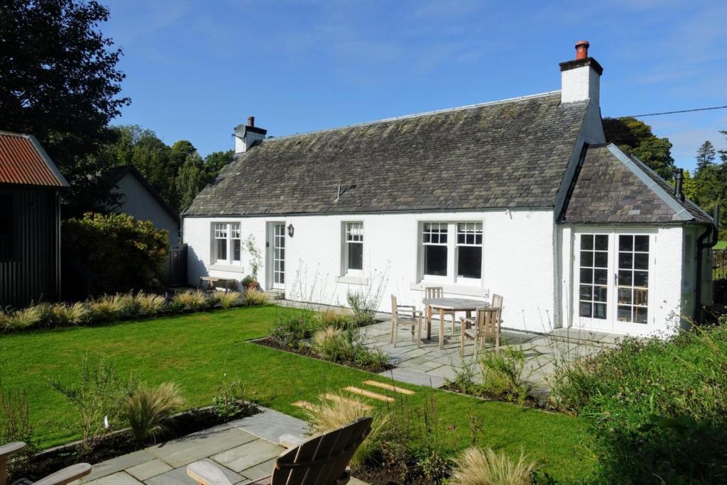 a white cottage with a table in the yard at Ross Lodge in Comrie