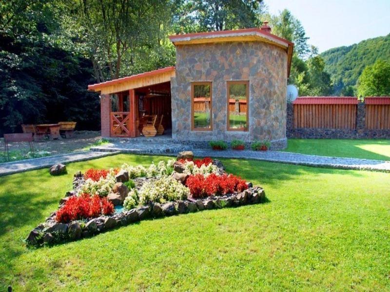 une petite maison avec un jardin fleuri dans la cour dans l'établissement Berloga, à Rodnikovka