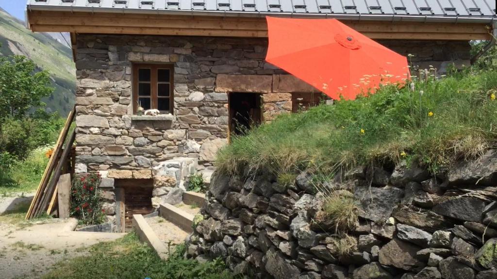 un parapluie rouge assis sur le côté d'une maison en pierre dans l'établissement Le Ptit Chalet, à Valloire