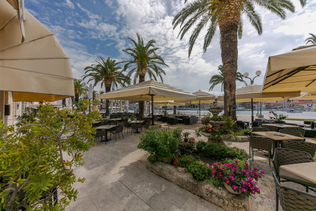 eine Terrasse mit Tischen, Sonnenschirmen und Palmen in der Unterkunft Hotel Concordia in Trogir