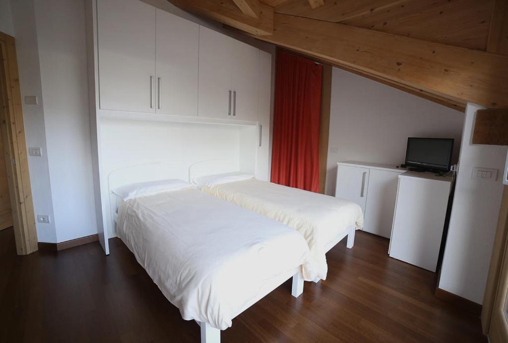 - une chambre avec 2 lits blancs et une télévision dans l'établissement Residence Rose, à Valdisotto
