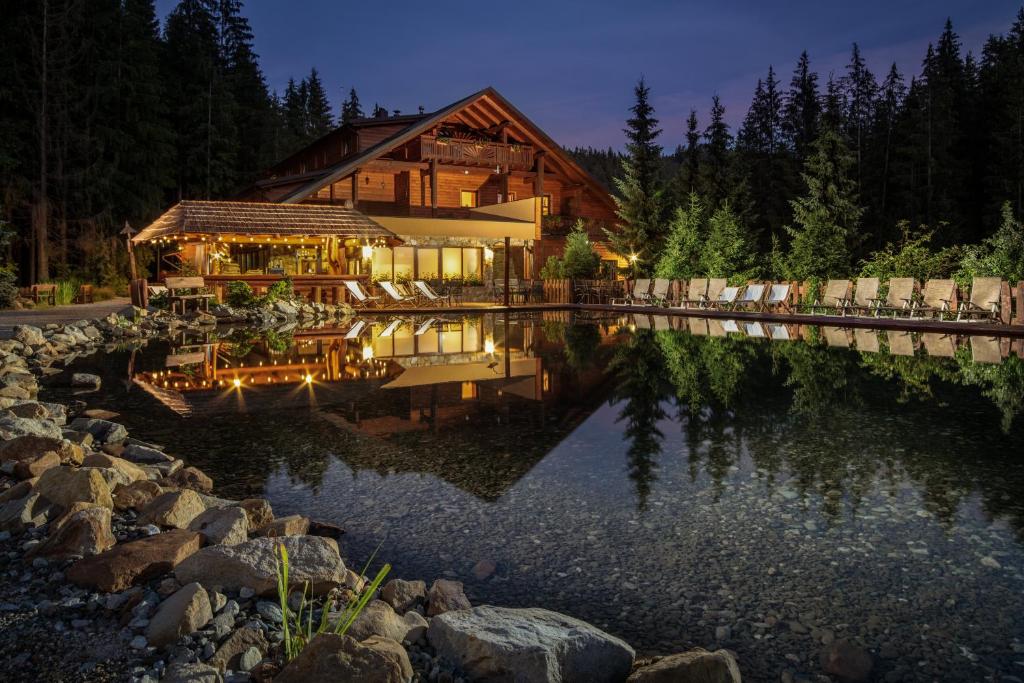 une maison en rondins avec un étang en face de celle-ci dans l'établissement Wellness Hotel Ondrášův dvůr, à Bílá