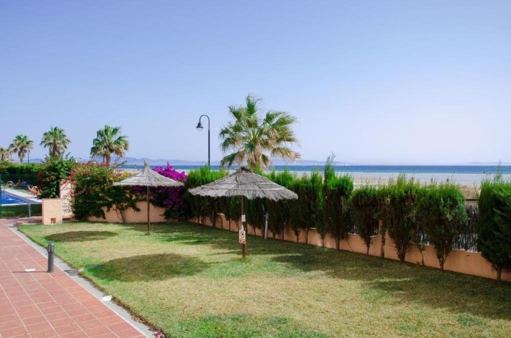 a garden with umbrellas and the beach in the background at Livingtarifa Apartamento Los Lances in Tarifa