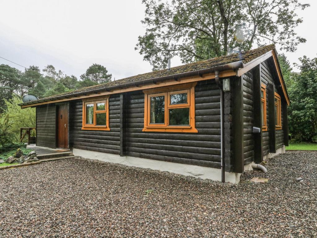 Cabaña de madera con ventanas de color naranja y grava en Millmore Cabin, en Killin