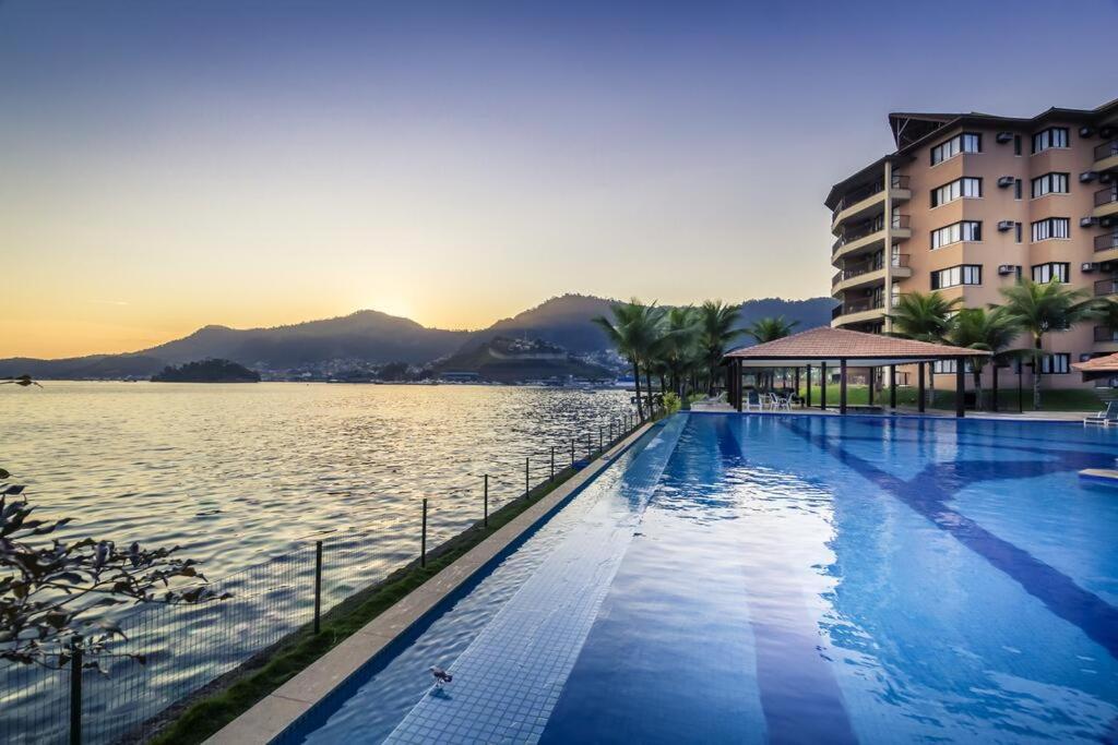 a large swimming pool next to a building and water at Angra dos Reis - Porto Bali - Apartamento no Complexo Mercur in Angra dos Reis