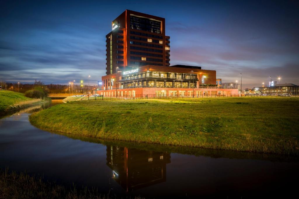Ein Gebäude wird nachts neben einem Fluss beleuchtet in der Unterkunft Van der Valk Hotel Dordrecht in Dordrecht