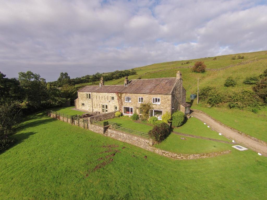 una casa vieja en una colina con un campo verde en Deerclose West Farmhouse en Leyburn