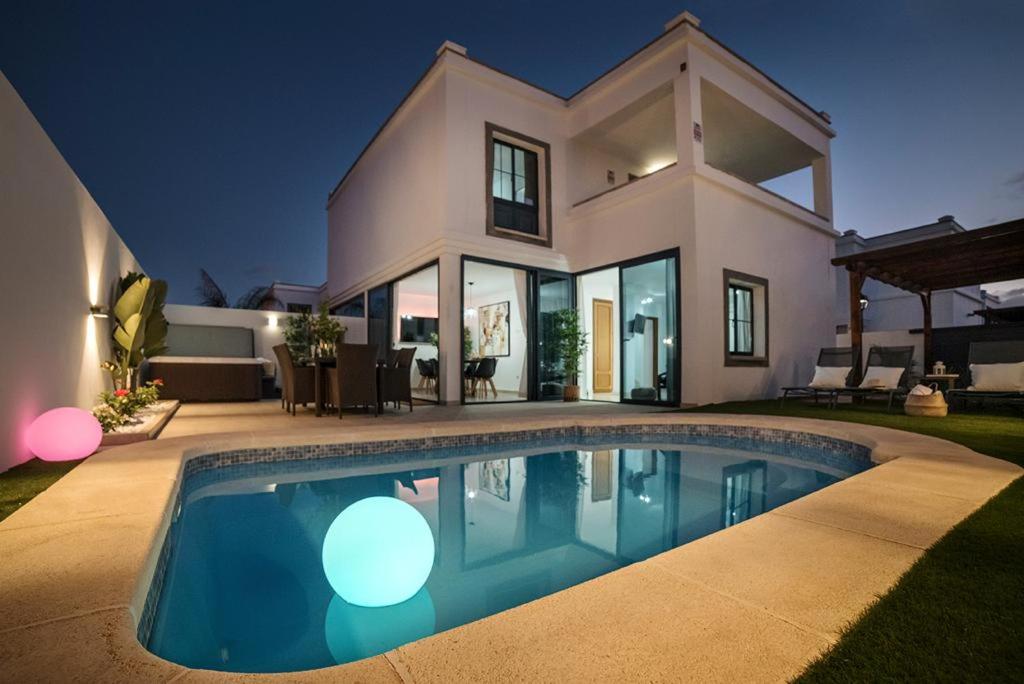 a house with a swimming pool in front of a house at Villa palmera jacuzzi in Yaiza