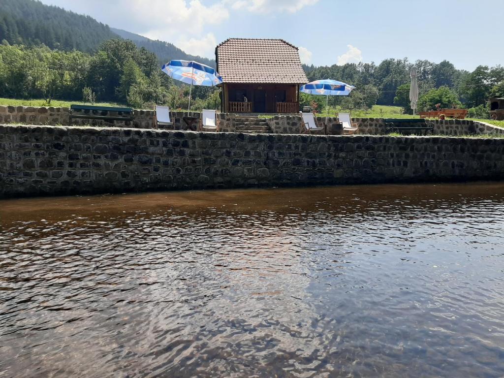 eine Steinmauer neben einem See mit einem Gebäude in der Unterkunft Apartman Šumska Tajna in Mokra Gora