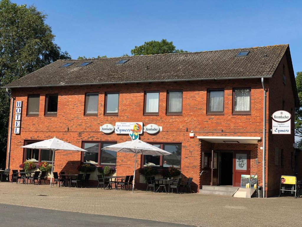 un edificio de ladrillo con mesas y sombrillas delante en Nordseehotel Eymers en Nordholz