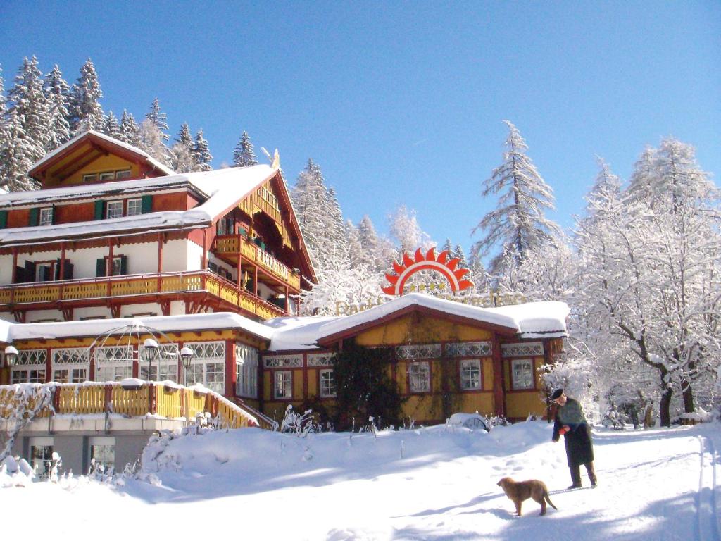 a man and a dog in the snow in front of a lodge at Parkhotel Sole Paradiso in San Candido