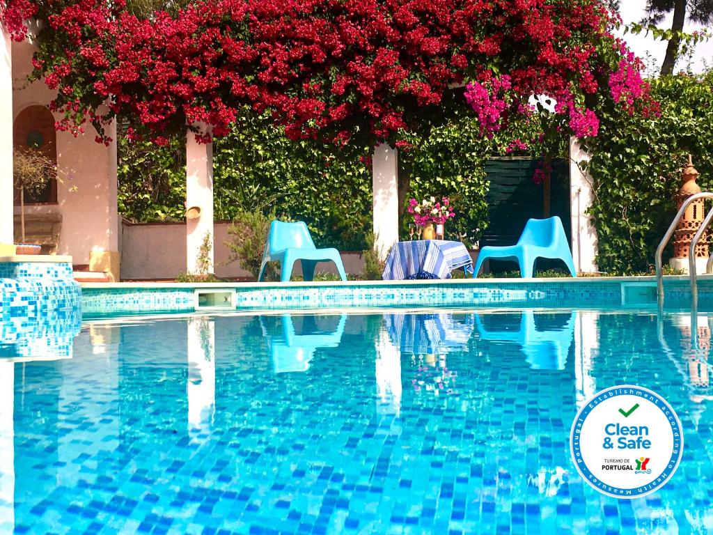 una piscina con sillas azules y flores rojas en Villa Canto da Lua, en Sesimbra