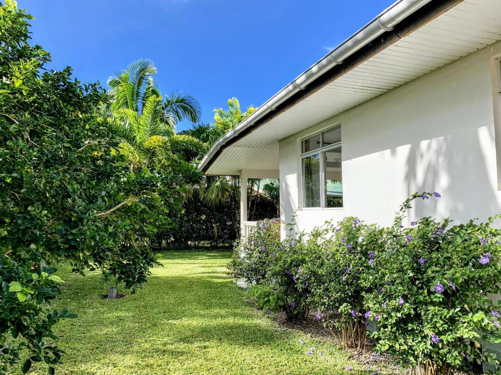 a white house with a yard with purple flowers at TAHITI - Fare Mitinui Surf Break in Mahina