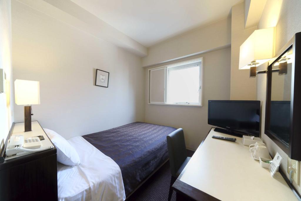 a hotel room with a bed and a desk and a television at Meitetsu Inn Nagoya Nishiki in Nagoya