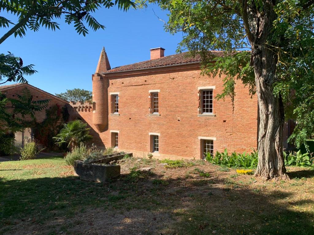 um velho edifício de tijolos com uma árvore em primeiro plano em Manoir du Bouyssou em Cintegabelle