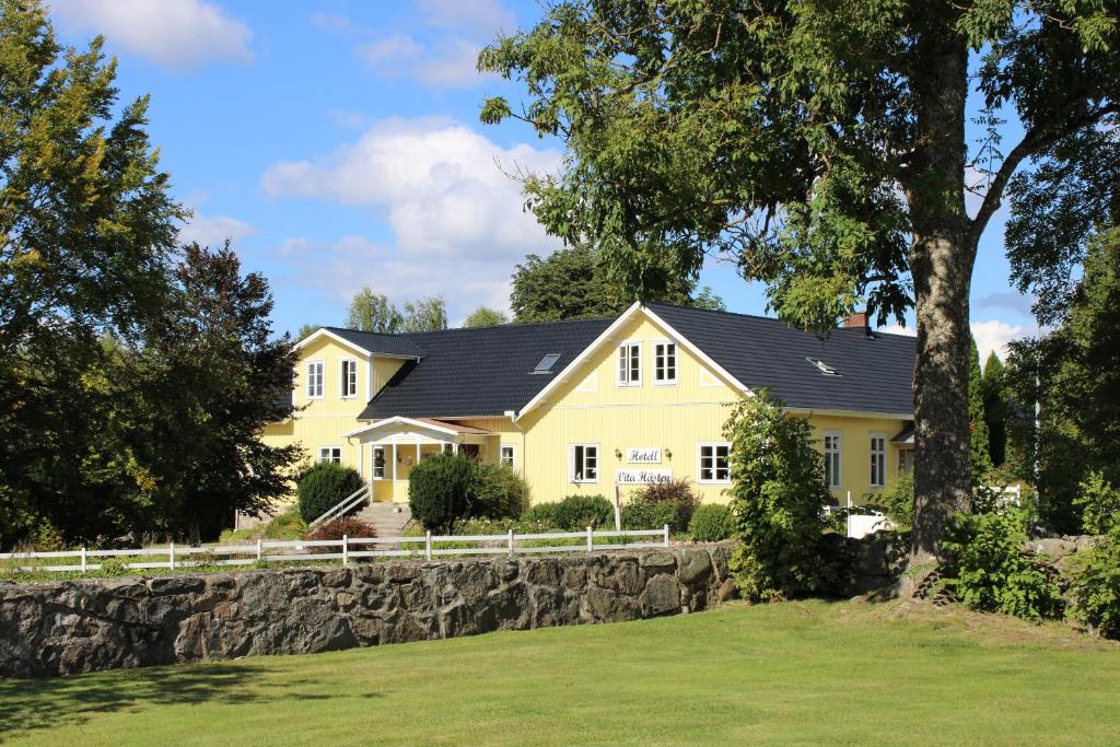 una casa amarilla con techo negro y pared de piedra en Hotell Vita Hästen Hästveda, en Hästveda