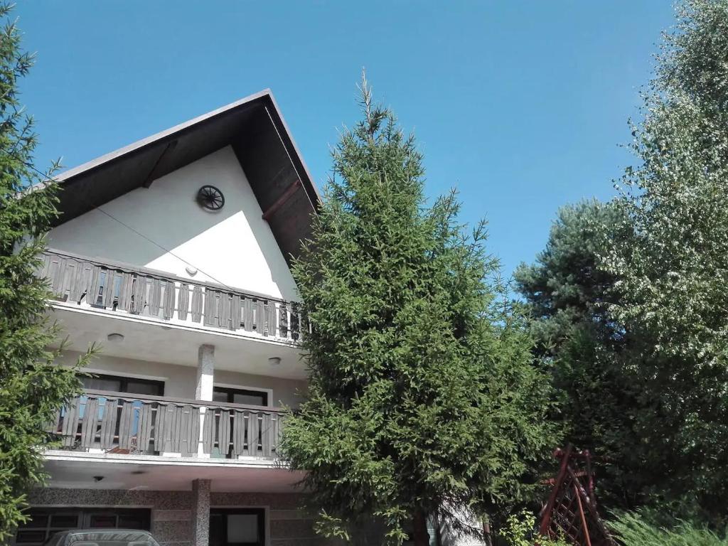 a white building with a balcony and two trees at Agroturystyka Janiczek Tuchów in Dąbrówka Tuchowska