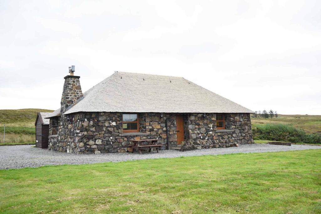 Struan的住宿－Crofters Cottage，一座石头建筑,在田野上设有屋顶