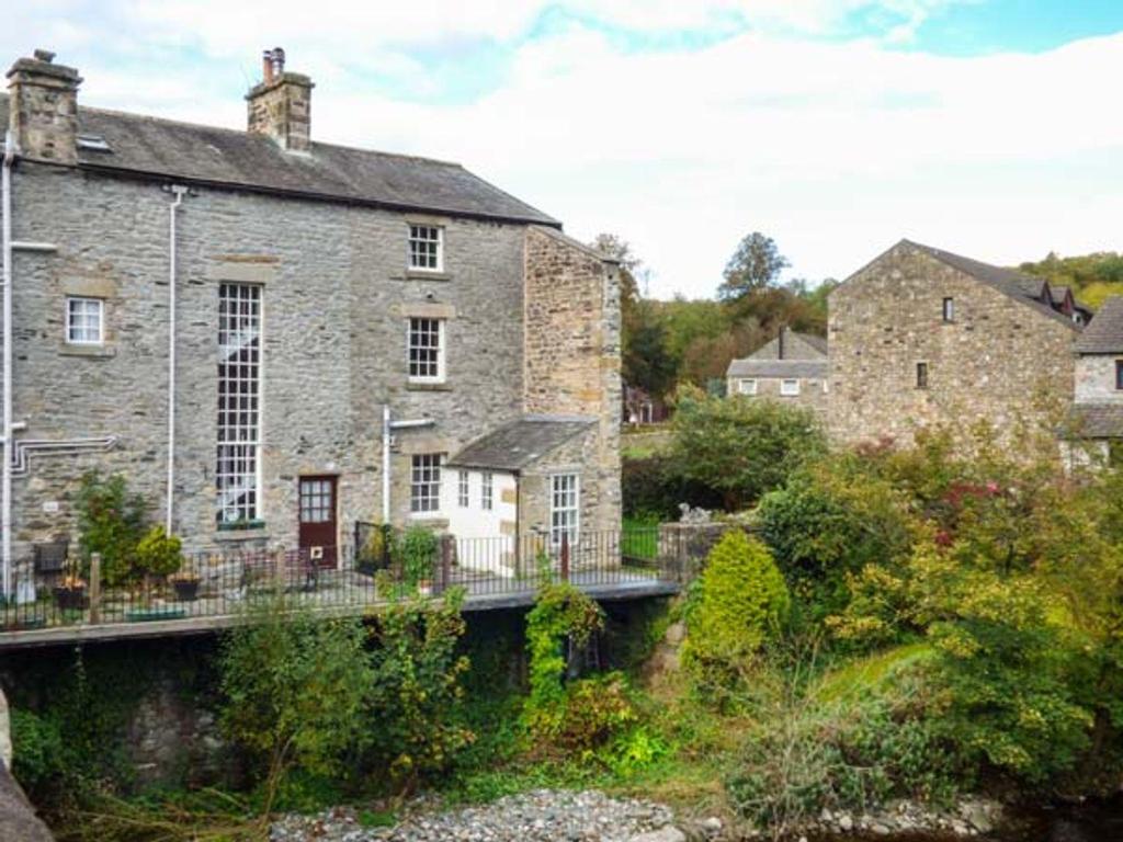 een oud stenen huis met een brug ervoor bij Bridge End Cottage in Carnforth