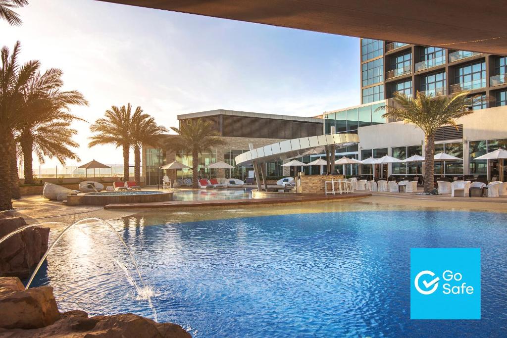 a swimming pool in front of a building with palm trees at Yas Island Rotana Abu Dhabi in Abu Dhabi