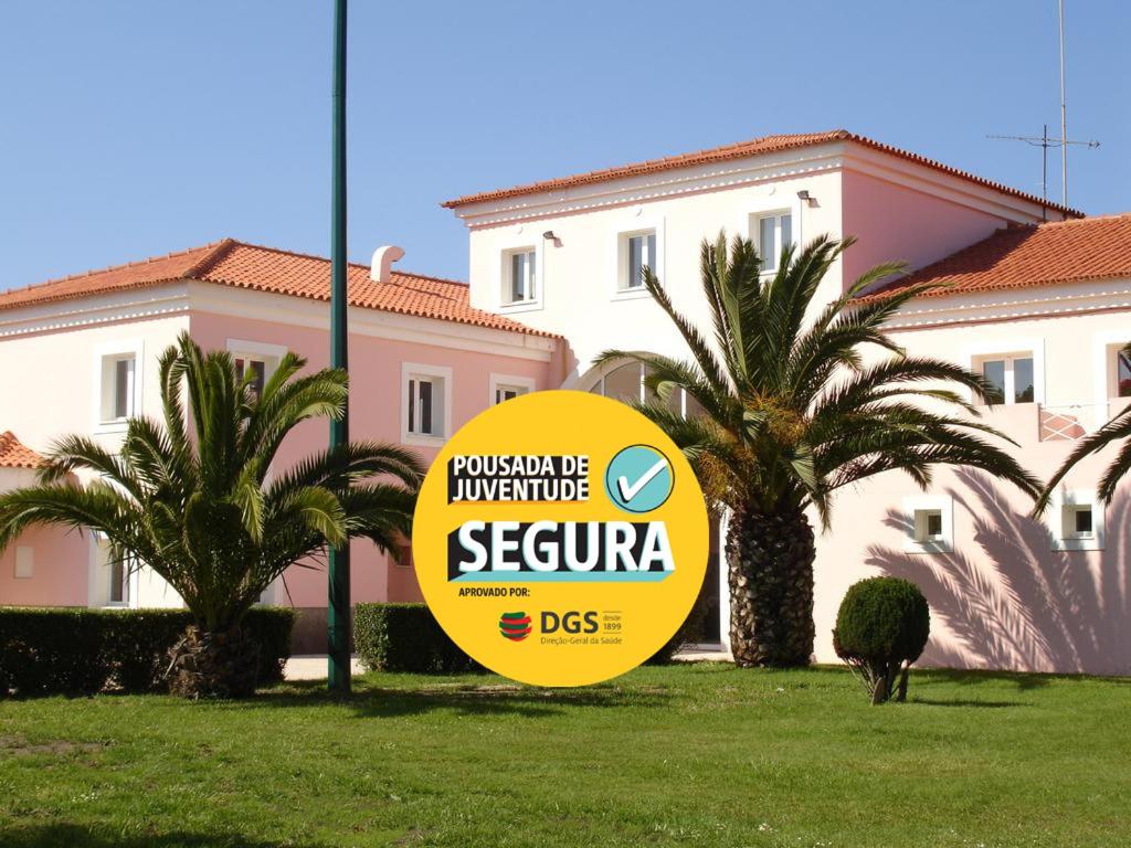 a yellow sign in front of a building with palm trees at HI Ofir – Pousada de Juventude in Esposende