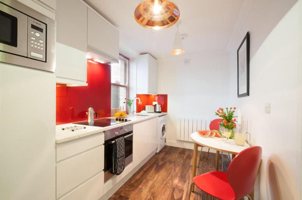 a kitchen with red and white cabinets and a table at Marylebone - Chiltern Street by Viridian Apartments in London