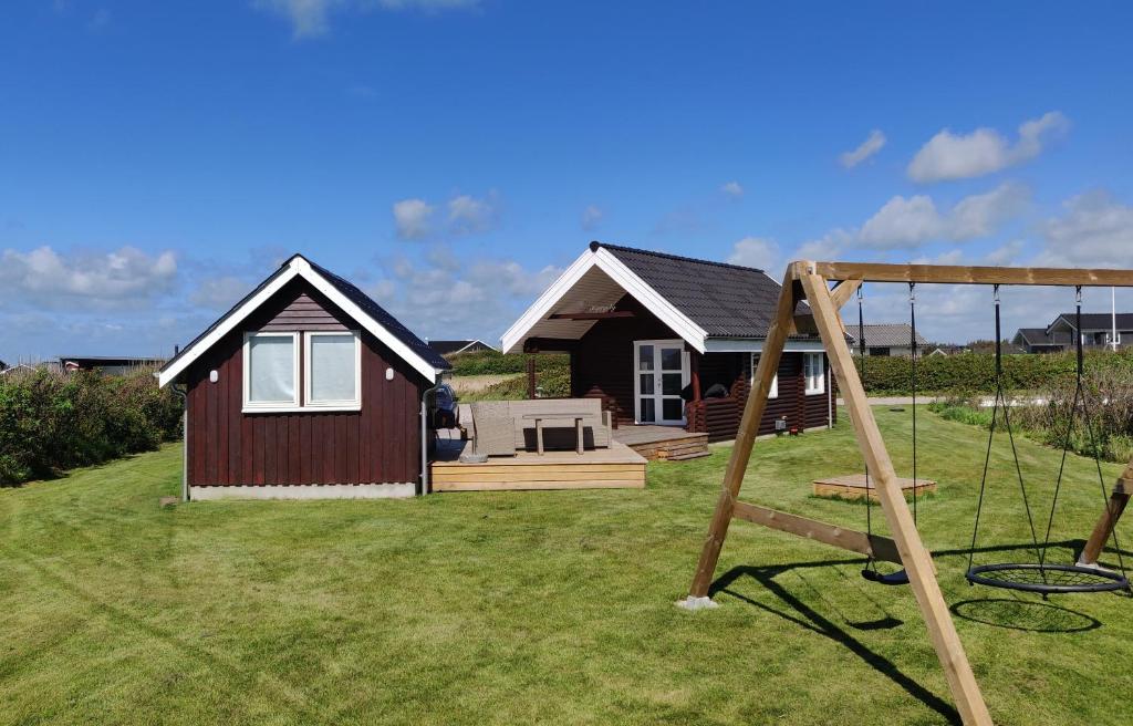 ein kleines Haus mit einem Spielplatz davor in der Unterkunft Hyggely - A Place By The Sea - Nørre Lyngby in Løkken