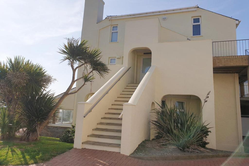 a white house with stairs and palm trees at 15 The CLIFF APARTMENT-2 BED- SEA VIEW in Trearddur