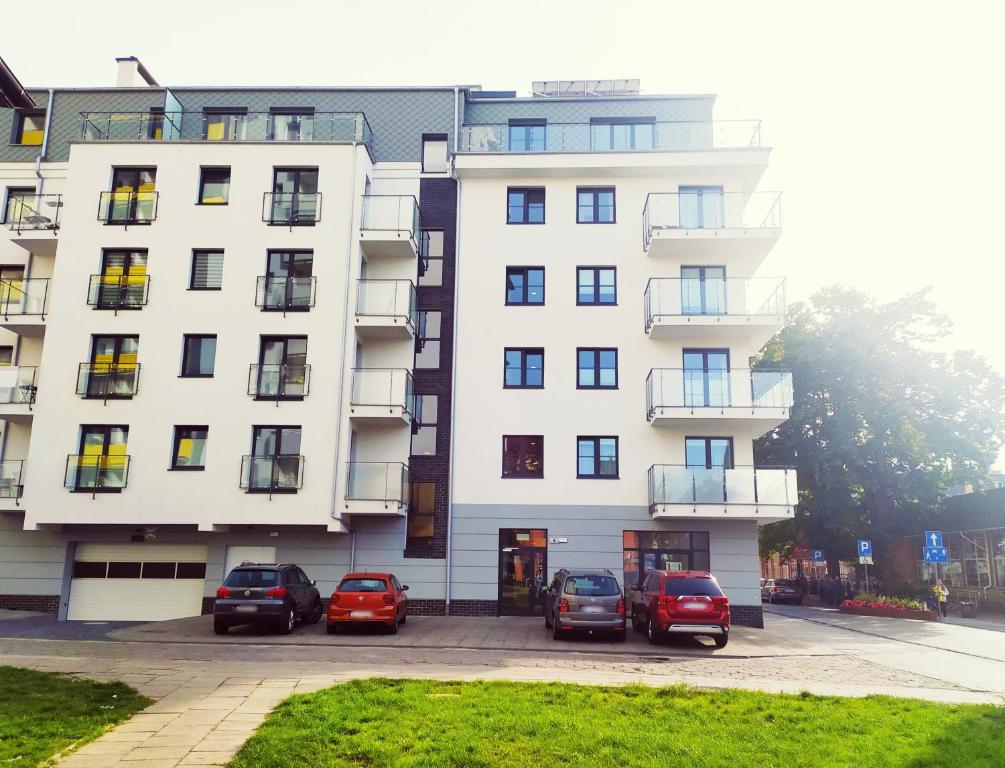 Biały budynek z samochodami zaparkowanymi przed nim w obiekcie Apartament Niebieski w Świnoujściu