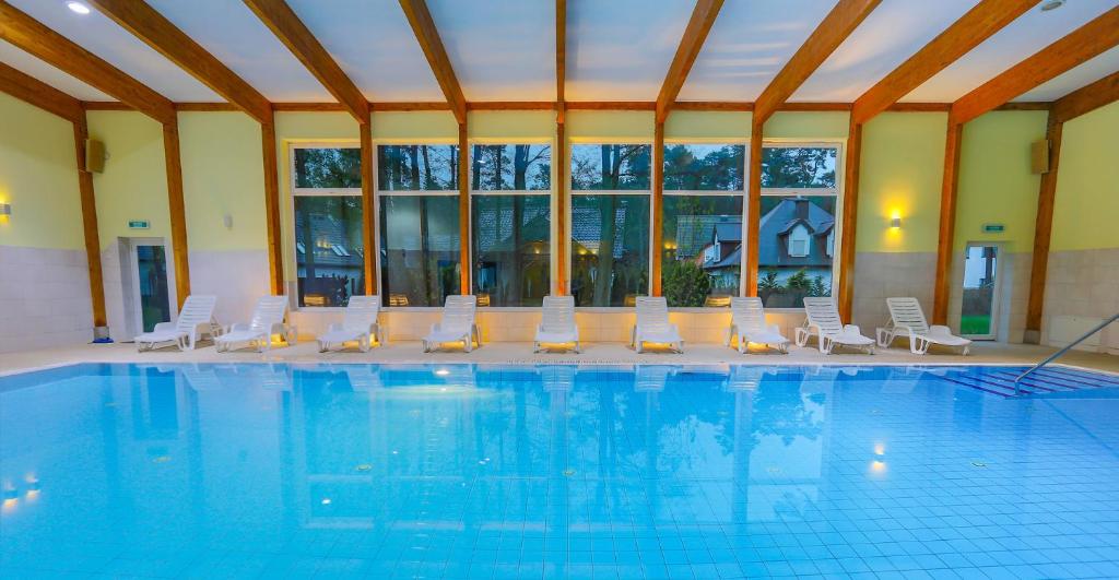 a swimming pool with white chairs and a large room at Millennium Health Resort & Spa in Międzywodzie