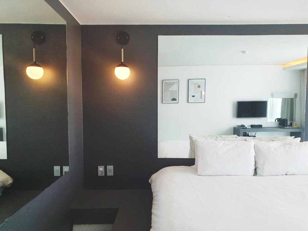 a bedroom with a bed with white pillows and two lights at Pampas Hotel Jeju in Jeju