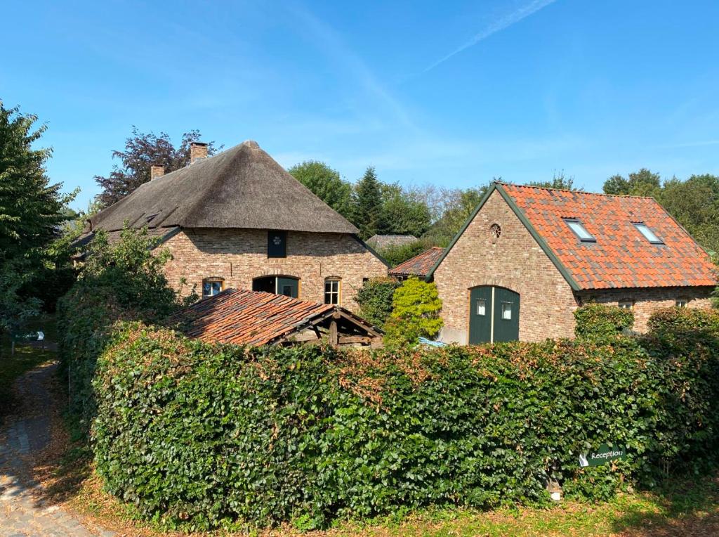 een oud huis met een rieten dak en een heg bij Hostel Kersenhof in Uden