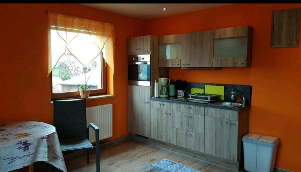 cocina con paredes de color naranja, mesa y ventana en Ferienzimmer im schönen Erzgebirge en Neuhausen