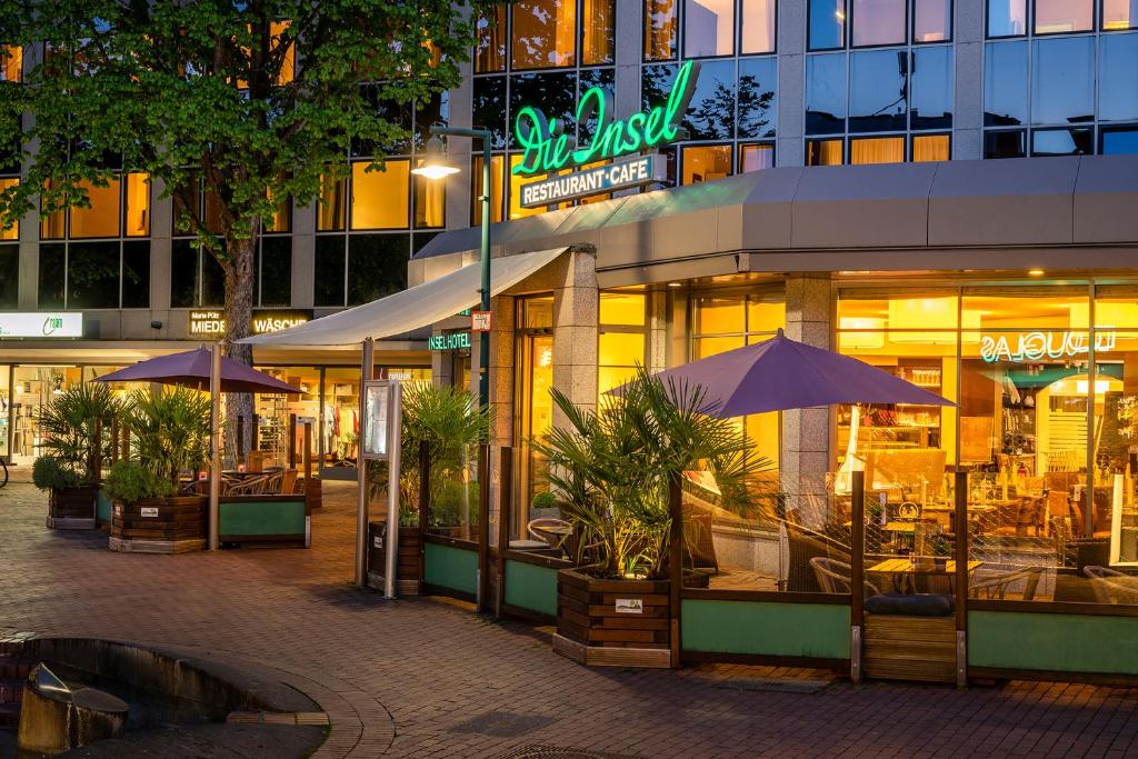 ein Restaurant mit Tischen und Sonnenschirmen vor einem Gebäude in der Unterkunft Insel Hotel Bonn - Superior in Bonn