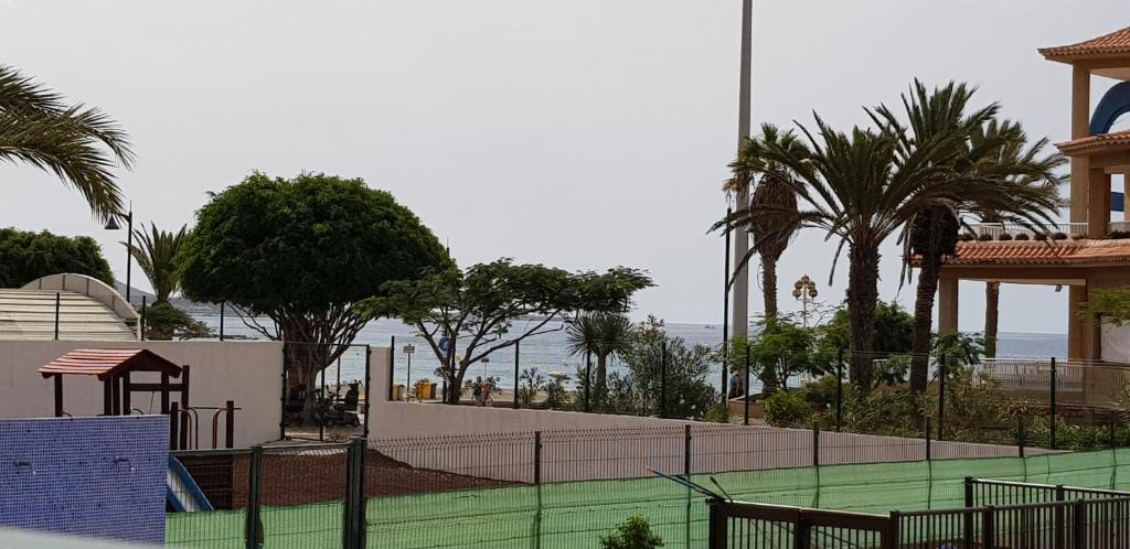 a tennis court with palm trees and the ocean at PLAYA LAS VISTAS LOFT in Los Cristianos