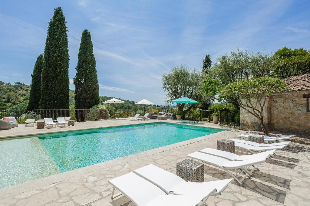 une piscine avec des chaises longues blanches et une villa dans l'établissement Le Manoir de L'Étang, à Mougins