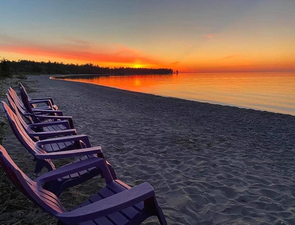 una fila di sedie a sdraio su una spiaggia al tramonto di The Purple Martin Lakeside Inn Bird Sanctuary on Lake Huron a Rogers City
