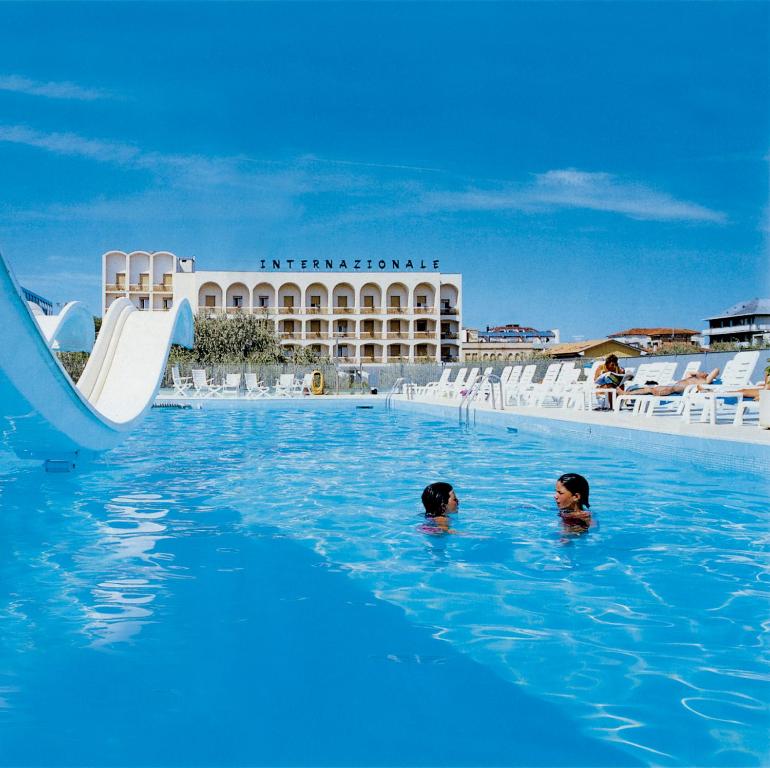 two people swimming in a swimming pool with a slide at Hotel Internazionale in Cesenatico