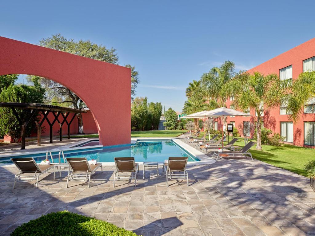 a swimming pool with chairs and a building at Fiesta Inn Aguascalientes in Aguascalientes
