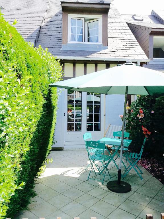 une table et des chaises sous un parasol devant une maison dans l'établissement Le Cottage, à Villers-sur-Mer