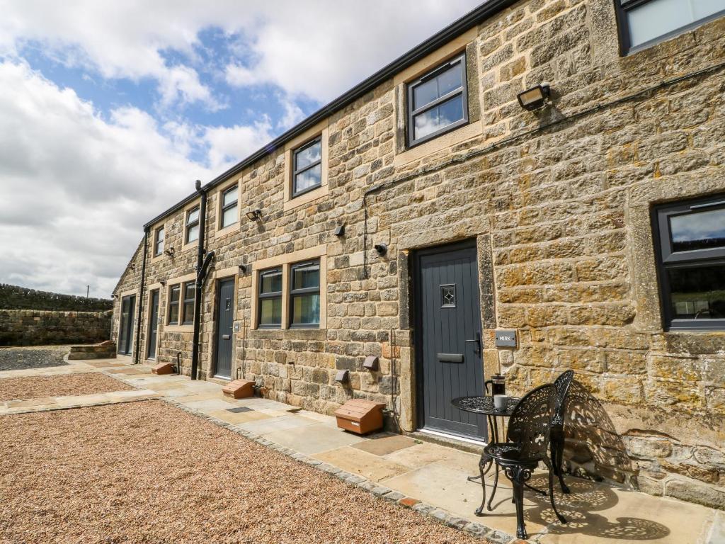 a brick building with a black door and a table at Mirk Cottage in Hebden Bridge