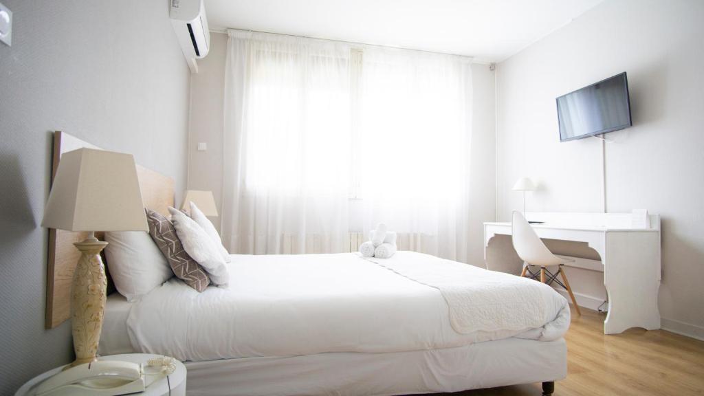 a white bedroom with a bed and a desk at Hôtel Pyrène in Foix