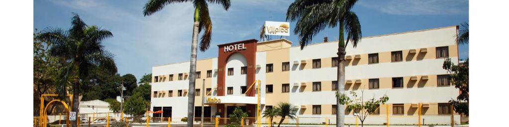a hotel with palm trees in front of a building at Villalba Hotel in Uberlândia