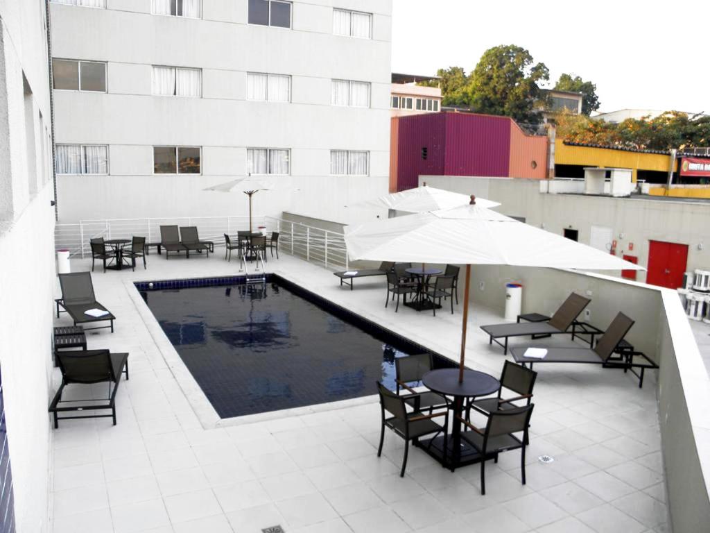 um pátio com mesas e cadeiras e uma piscina num edifício em Nobile Inn Dutra Rio De Janeiro em São João de Meriti