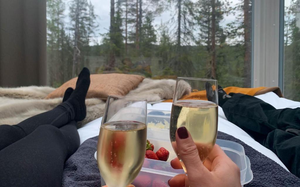 Zwei Leute halten Champagner-Gläser auf dem Bett. in der Unterkunft Arctic Skylight Lodge in Äkäslompolo