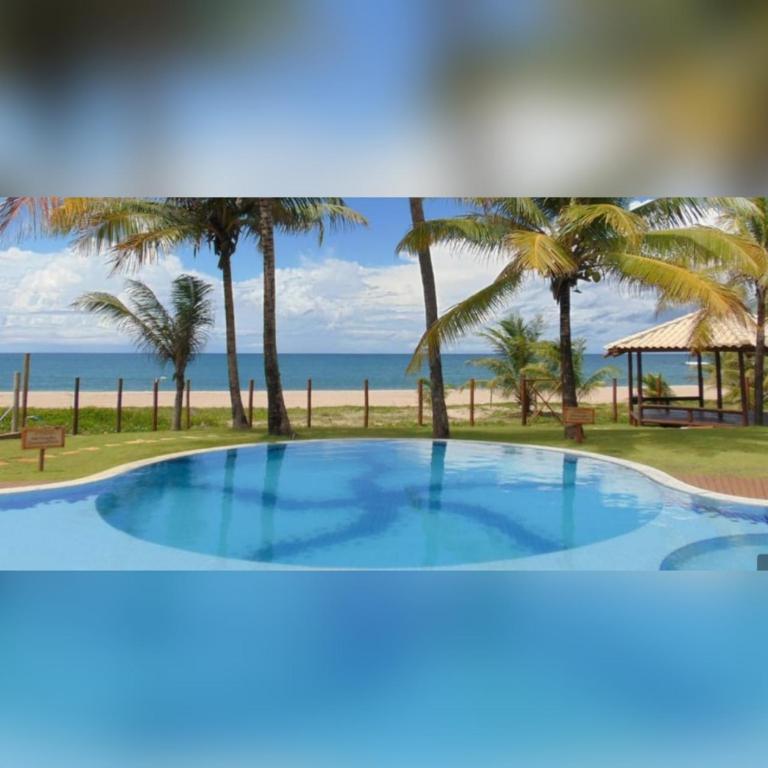 a large swimming pool with palm trees and the beach at Village AREIAS ITACIMIRIM - PÉ NA AREIA in Itacimirim
